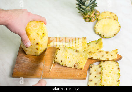 Männliche Hände schneiden frischen Ananas auf einem Holzbrett Stockfoto