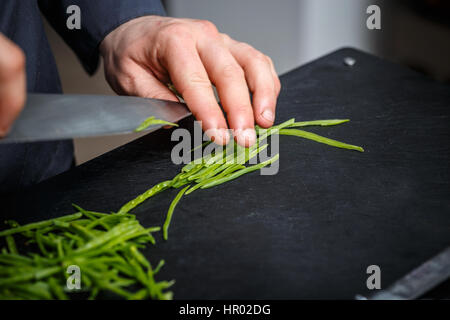 Koch schneiden frische grüne Erbse auf die schwarze Schneidebrett Stockfoto