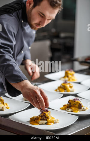Junger Koch bereitet köstliche Mahlzeiten im Restaurantküche. Stockfoto