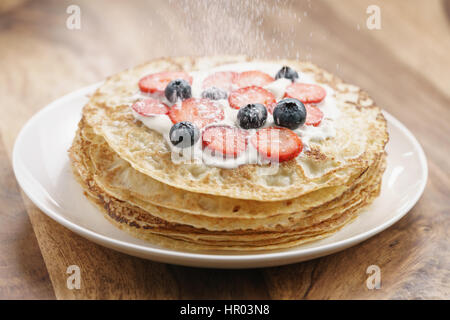 auf frischen Blinis oder Crepes mit frischen Beeren und Sahne, süße Lebensmittel Zucker Pulver fallen Stockfoto