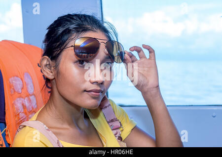 Frau mit Sonnenbrille sitzt auf einem Schiff neben Fenster mit Blick auf den See. Frau Passagier Reisen in eine Fähre auf dem Meer. Stockfoto