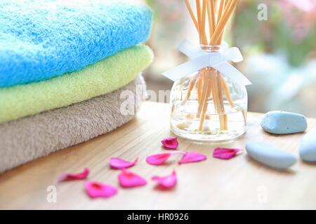 Aromatherapie Reed Diffuser Flasche auf einem Holztisch mit Handtüchern, Blüten und Steinen massage Stockfoto
