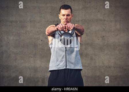 Junge sportliche konzentriert Mann Hände nach vorne mit schweren Kettlebell ausstreckten und Blick in die Kamera. Stockfoto