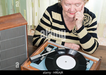 Die ältere Frau sitzt am Tisch und Retro-Musik hören von einem Vintage Plattenspieler Stockfoto