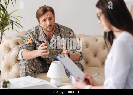 Posttraumatische Belastungsstörung. Deprimiert hübscher junger Soldat mit Blick auf seine Psychologin und erzählt ihr über seine Probleme beim haben einer posttrau Stockfoto