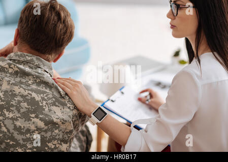 Ich unterstütze Sie. Angenehme schöne weibliche Psychologe legte ihre Hand auf die Soldaten Schulter und ihn zu unterstützen, während Sie mit einer psychologischen Sitzung Stockfoto