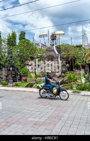 UBUD, Indonesien - 29. August 2008: Junge Mädchen reitet Motorrad auf der Straße in der Nähe von den Statuen der Dämonen Stockfoto