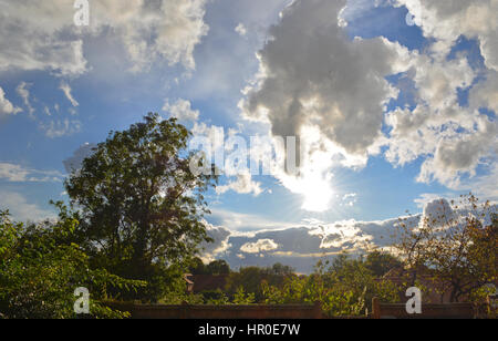Flauschige weiße Wolkengebilde über ländlichen englischen Gärten und Häuser mit einem Baum im Hochsommer Laub. Stockfoto