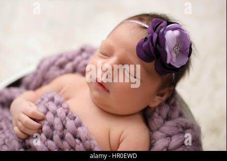 Neun Tage alten neugeborenen Mädchen schläft in einem Holzeimer. Sie trägt eine Stirnband Lavendel und lila Blume. Stockfoto