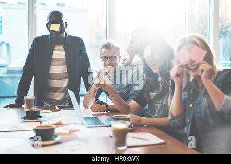 Gruppe von Jugendlichen im Café Spaß Spiel Name mit Haftnotizen auf ihre Stirn, gegen die großen hellen Fenster Stockfoto