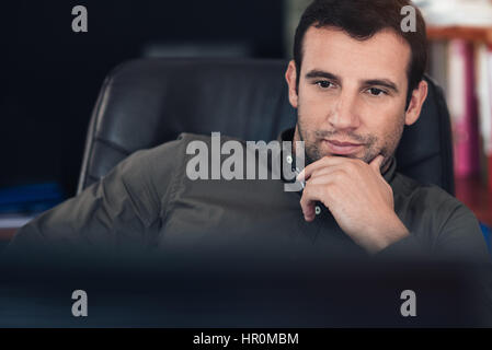 Fokussierter junger Geschäftsmann, sitzen an einem Schreibtisch tief in Gedanken während der Arbeit an einem Computer an einem Schreibtisch in einem Büro Stockfoto