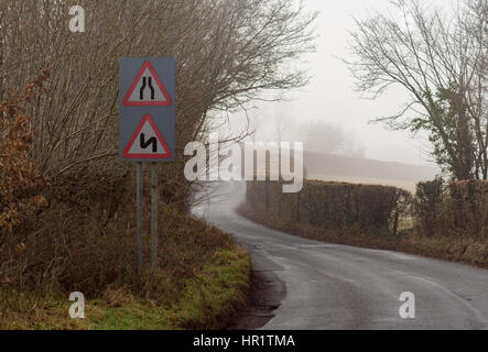 Straße verengt und Doppel beugt sich zuerst auf der linken Seite, auf einer Straße in Wales mit leichten Winternebel. In der Nähe der Siedlung Glanusk in Brecon Nationalpark Stockfoto