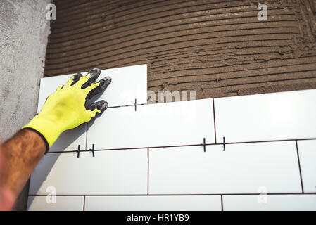 Industriearbeiter holding Keramikfliesen und Zement Kleberauftrag auf Badezimmerwänden Stockfoto