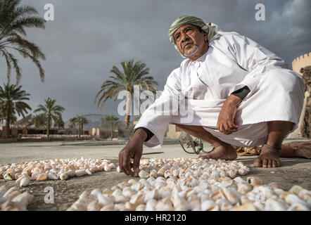 Muscat, Oman - 4. Februar 2017: Ein traditionell gekleideten omanischen Mann auslegen Muscheln an einem bewölkten Tag. Stockfoto