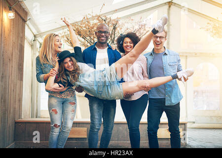 Junges Mädchen in Hut und Denim-Overalls Handauflegen Arme Freunde, posiert in die Kamera, Lächeln und Spaß, Gruppe stehen im Innenbereich Stockfoto