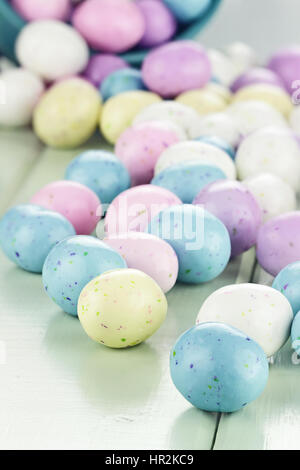 Eine blaue Blecheimer umgekippt, verschütten Süßigkeiten Ostereier auf einen Tisch. Geringe Schärfentiefe mit selektiven Fokus auf engsten Süßigkeiten Eiern. Stockfoto