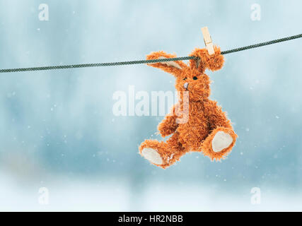 traurige kleine Spielzeug Hase hängen an einem Seil im Schnee Stockfoto