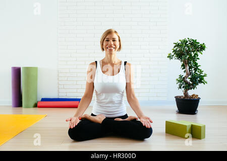 Frau beim Yoga im Studio-Lotus-Position mit einem charmanten Lächeln Stockfoto