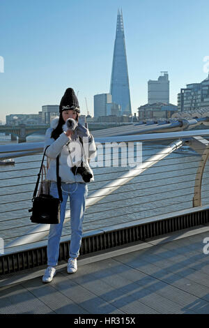 Junge Frau, die eine Selfie an einem sonnigen Wintertag auf Millennium Bridge & Blick auf den Shard Gebäude in South London England UK KATHY DEWITT Stockfoto
