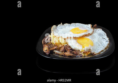 Spiegeleier mit Kartoffeln und Champignons auf einem schwarzen Hintergrund. Stockfoto