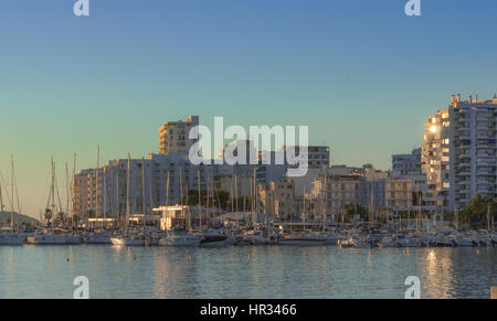 Späten Nachmittag Sonne fällt auf Marina Promenade & Bucht in St. Antoni de Portmany, Ibiza, Balearic Isl & s, Spanien.  Sonne Schimmer aus Eigentumswohnung Bauglas. Stockfoto