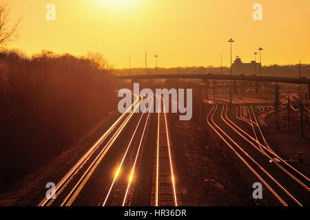 Die untergehende Sonne aus Burlington Northern Santa Fe und Metra Bahngleise in Aurora, Illinois, USA widerspiegelt. Stockfoto