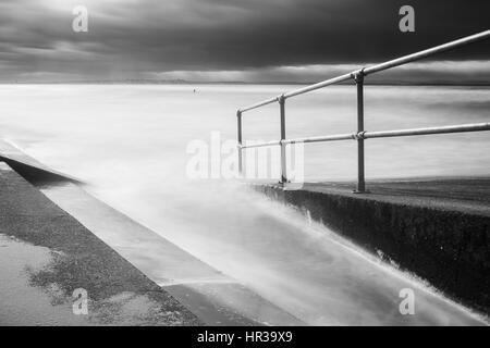 Das Wasser des Meeres stürmt auf der Helling & Beibehaltung der Ufermauer an der Sefton Küste in der Nähe von Liverpool unter einige dramatischen Wolken.  Ein einsamer Kopf ein sta Stockfoto