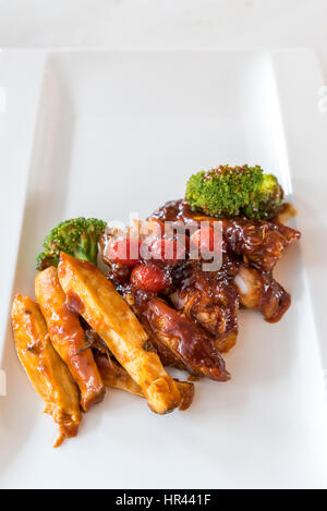 Schweinefleisch Rippe gegrillte und gebratene Kartoffelspalten auf weißen Teller mit Sauce und Gemüse, Gourmet-Küche. Stockfoto