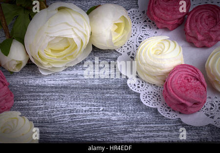 Weißer Hahnenfuß Blumen Ranunkeln weiß und rosa Zephyr Marshmallows lacy Papierserviette auf grauem Hintergrund aus Holz. Textfreiraum Stockfoto