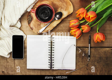 Overhead Schuss einen Strauß Blumen, Kaffee, ein offenes Buch und Handy über eine hölzerne Tischplatte bereit, eine Agenda zu planen. Flache Laien Draufsicht Stil. Stockfoto