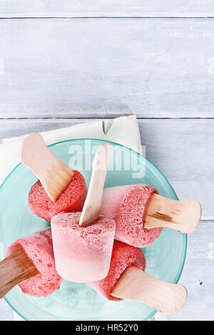 Erdbeer Eis am Stiel über eine hölzerne Tischplatte aus Erdbeeren und Joghurt hergestellt. Erschossen von oben. Stockfoto