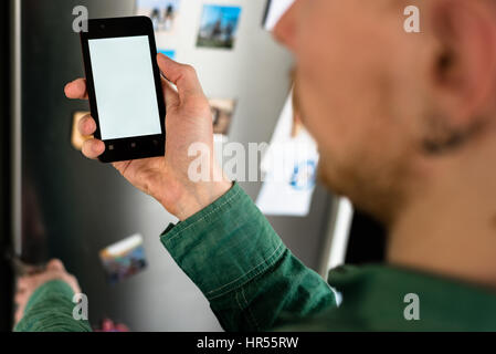 Nahaufnahme der Person Hände halten Smartphone zeigt leere Seite auf dem Bildschirm. Kühlschrank auf Hintergrund Stockfoto