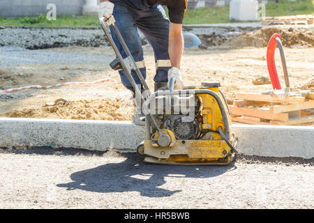 Worker nutzen Vibrations Platte Verdichter komprimiert Asphalt bei Straßenreparatur Stockfoto