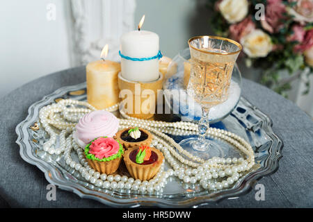 Kerzen, Kuchen, Perlen auf dem Silbertablett während der Hochzeit. Stockfoto