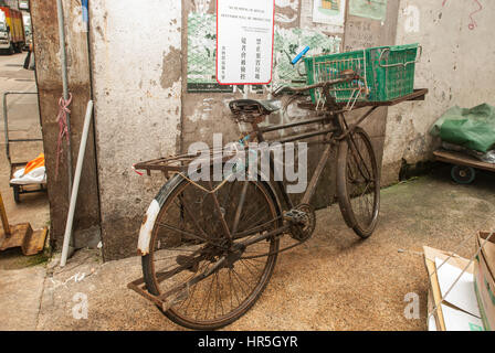 Verrostete altes Fahrrad mit grünen Korb lehnt sich an die Wand, Hong Kong, China. Stockfoto