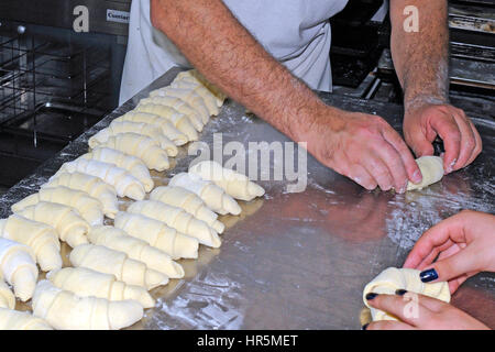 Ein Bäcker arbeiten auf einer bemehlten Arbeitsfläche aufrollen Teig Quadrate in Croissant Formen vor dem Backen Stockfoto