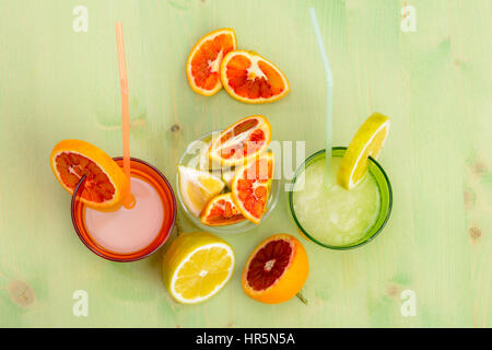 Saft einer Zitrone und Orange mit FRUCHTSCHEIBEN auf einem grünen Tisch und rotem Hintergrund Stockfoto