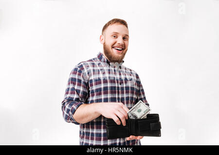 Glücklicher bärtiger Mann im Hemd bringt Geld in die Geldbörse im Studio. Isolierten weißen Hintergrund Stockfoto
