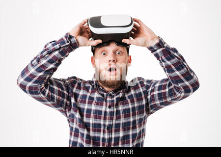 Überraschter, bärtiger Mann im Hemd startet virtuelle Realität Gerät mit offenem Mund und Blick in die Kamera. Isolierten weißen Hintergrund Stockfoto