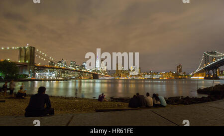 Junge Menschen entspannen Sie sich auf das Vorland von Pebble Beach in Main Street Park mit Brooklyn und Manhattan Bridge und Wolkenkratzer eine bunte Kulisse Stockfoto