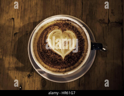 Tasse Kaffee auf einer hölzernen Tischplatte, genommen von oben, herzförmige Schaum oben auf den Kaffee, gedeckte Farben getönt Stockfoto