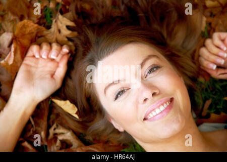 schöne Herbst Frau lächelnd auf den Boden, umgeben von verlässt Stockfoto