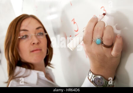 weibliche Lehrer schriftlich auf einer Tafel während einer Unterrichtsstunde Mathematik - über einen weißen Hintergrund mit dem Fokus auf ihre hand Stockfoto