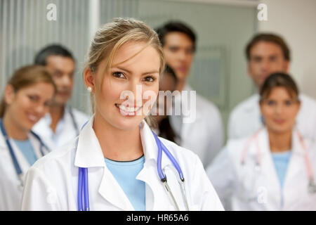 Ärztin in einem Krankenhaus mit ihrem Team hinter Lächeln Stockfoto