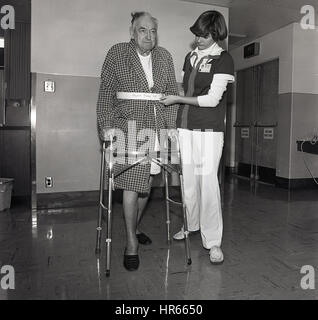 1960, historische, Physikalische Therapie, eine weibliche Krankenschwester hilft ein älterer Mann in-Patient in einem Krankenhaus Flur kleine Schritte mit Hilfe eines Metall Zimmer Typ frame seine Bewegung, USA zu unterstützen. Stockfoto