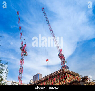 Zwei rote Bau Krane Strecke bis in den bewölkten blauen Himmel. Stockfoto