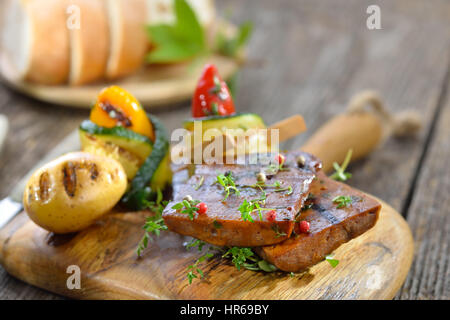 Vegetarische Grillplatte mit veganen Seitan Scheiben Brötchen Zucchini mit Paprika und gegrillte Kartoffeln Stockfoto