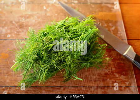 Zweige frischer grüner Dill mit Wasser Tropfen auf einem Holztisch. Großen metallischen Messer auf einen natürlichen Hintergrund. Selektiven Fokus. Stockfoto