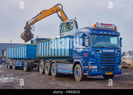 Ein Kran mit hydraulisch angehoben Kabine und ausgestattet mit einer Sortierung Greifer wird einen Container auf LKW-Anhänger mit Schutt geladen. Erste Container im Mittelpunkt. Stockfoto