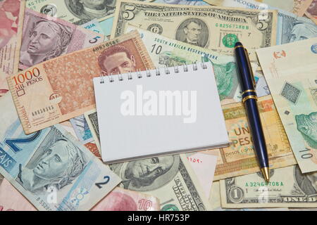 Leere Notizbuchseite mit Stift auf Hintergrund von Währungen der Welt Stockfoto